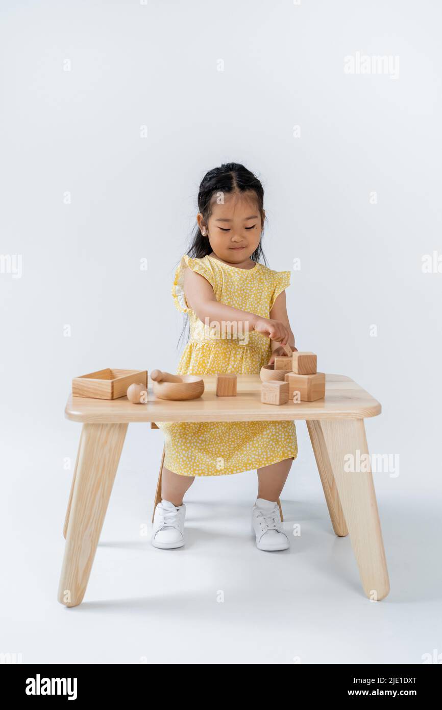 full length of asian child playing with wooden toys on table on grey Stock Photo