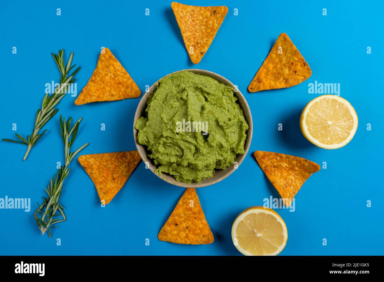 Composition of guacamole with the ingredients for its creation and the nachos for its consumption on a blue background Stock Photo