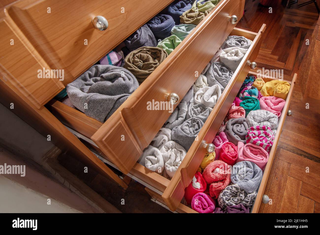 Open chest drawers with vertical storaged twisting clothes. View from
