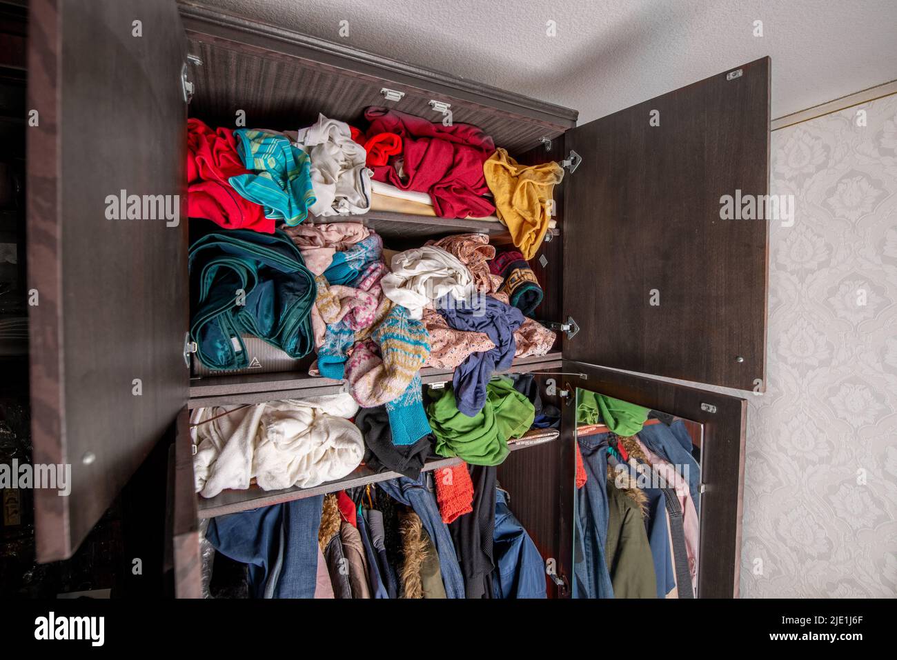 Open wardrobe with clothes on hangers and clutter in open drawers Stock