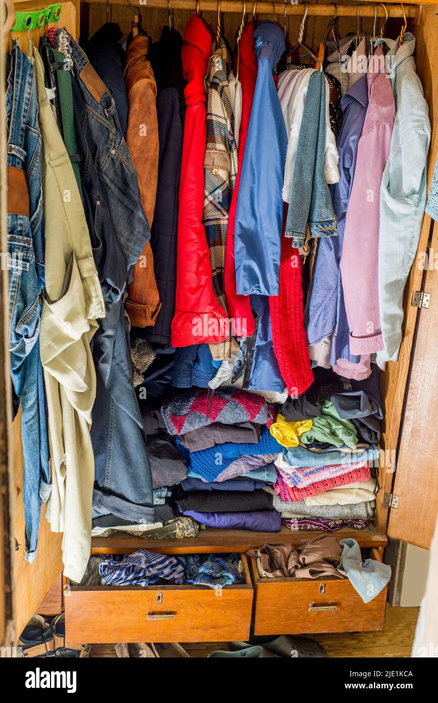 Old and new clothes in the closet on hangers and drawers. Second hand reuse. Decluttering and cleaning the cabinet Stock Photo