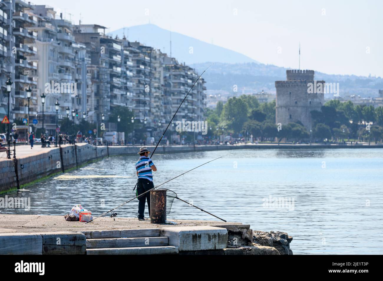 A fisherman on Thessaloniki waterfront with Nikis Avenue and the white Tower in the background, Macedonia, Northern Greece Stock Photo