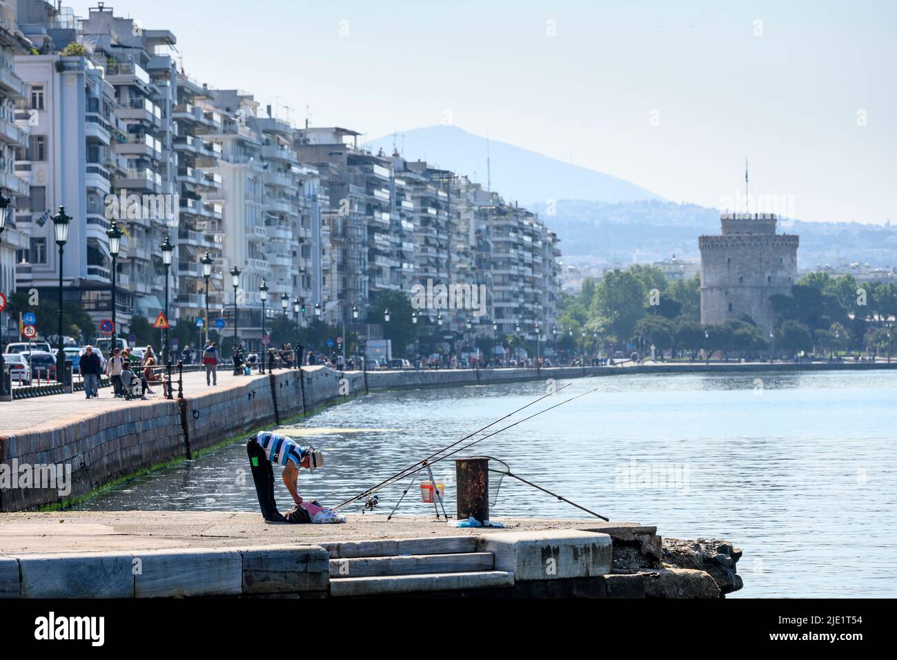 A fisherman on Thessaloniki waterfront with Nikis Avenue and the white Tower in the background, Macedonia, Northern Greece Stock Photo