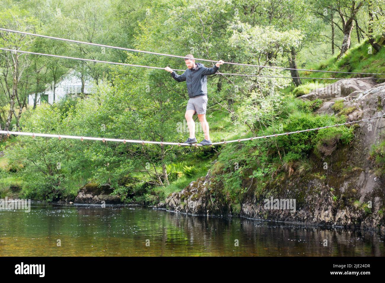 Man walking across Steall wire bridge over Water of Nevis river with Steall Falls Stock Photo