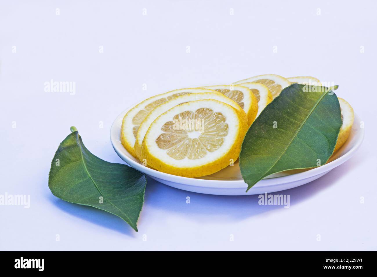 Sliced lemons and green leaves on a white plate isolated on white background Stock Photo
