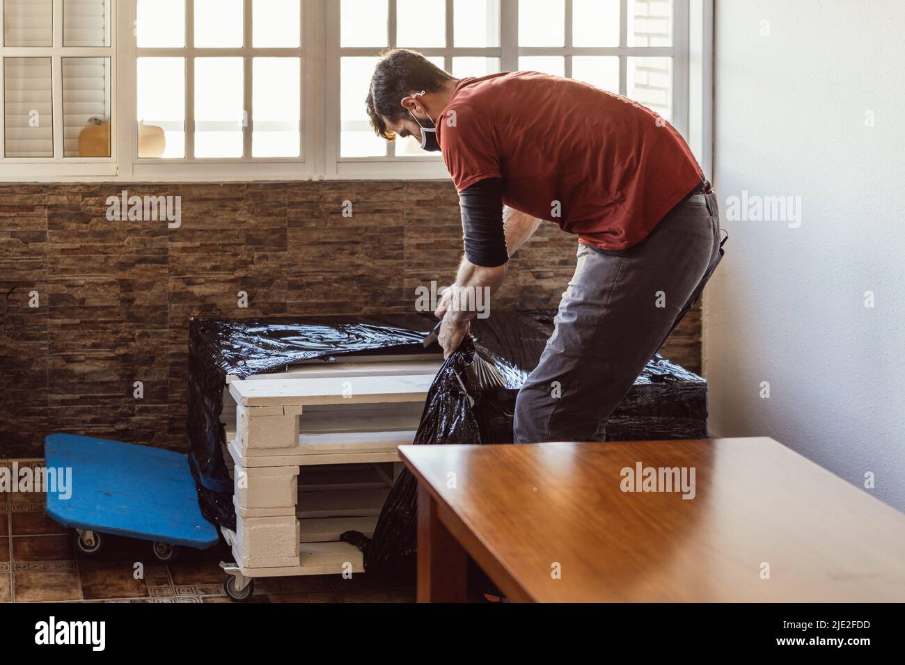 worker removing plastic wrap from a piece of furniture in a moving operation Stock Photo