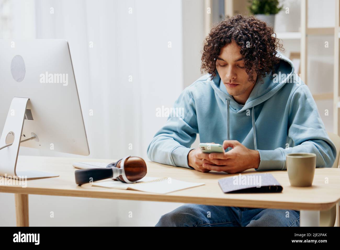 Guy With Curly Hair In A Blue Jacket In Front Of A Computer With Phone 