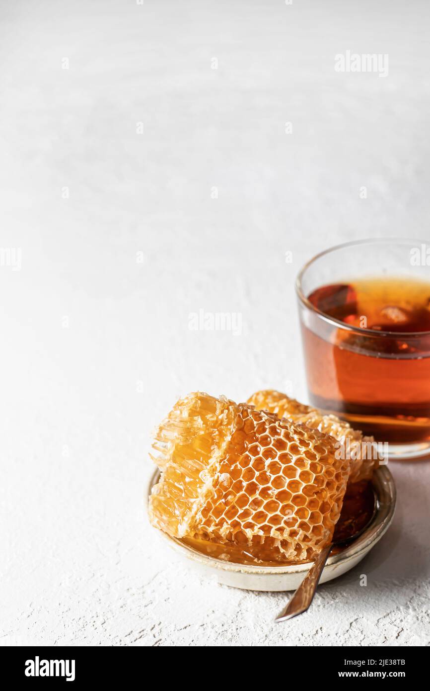 Honey in Honeycomb in a saucer with spoon and cup of tea on a white