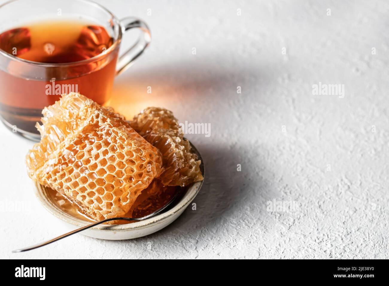 Honey in Honeycomb in a saucer with spoon and cup of tea on a white