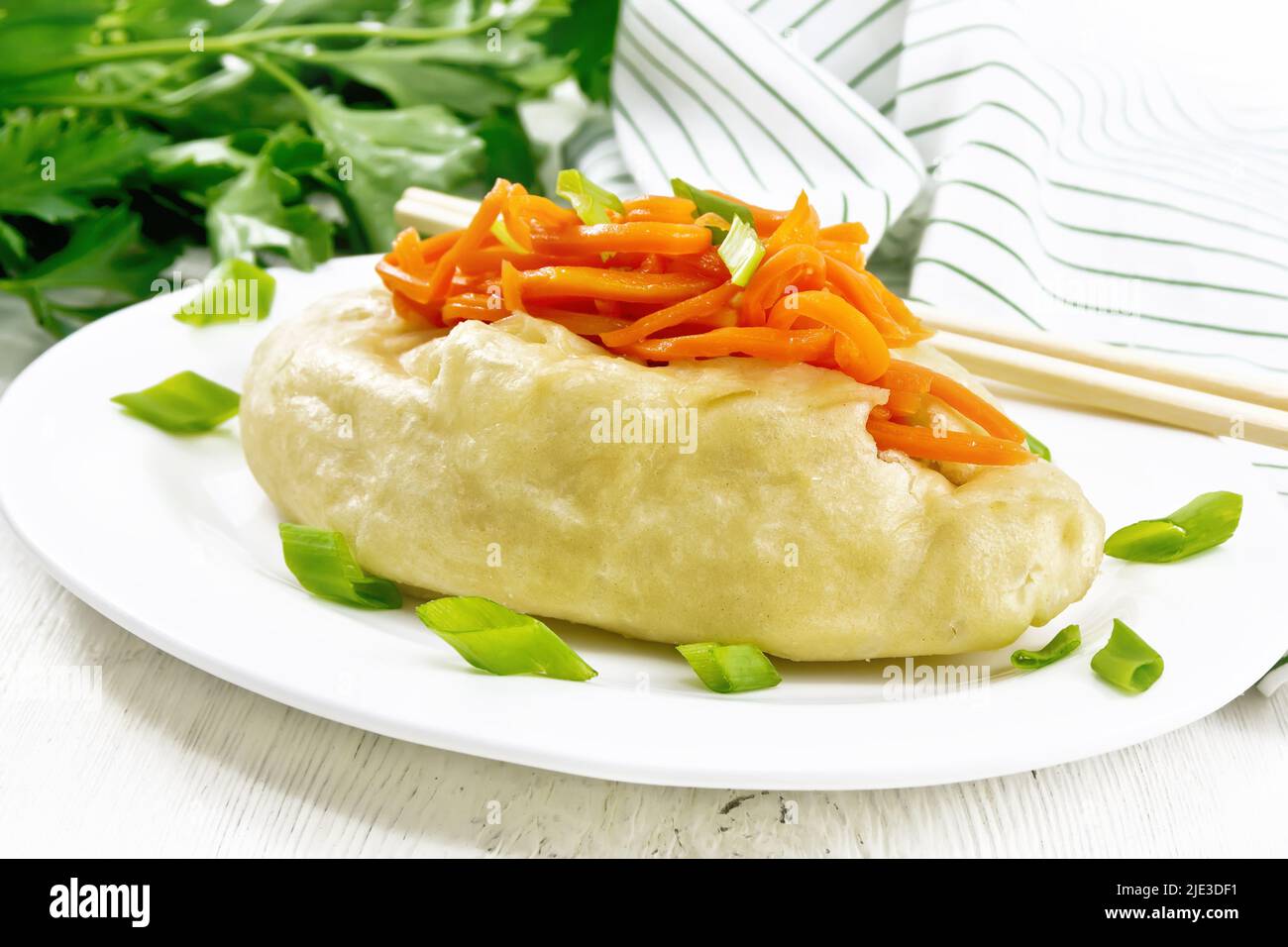 Pegodi patty with stewed cabbage and meat, steamed, seasoned with spicy carrots and green onions in a plate, napkin and parsley on a light wooden boar Stock Photo