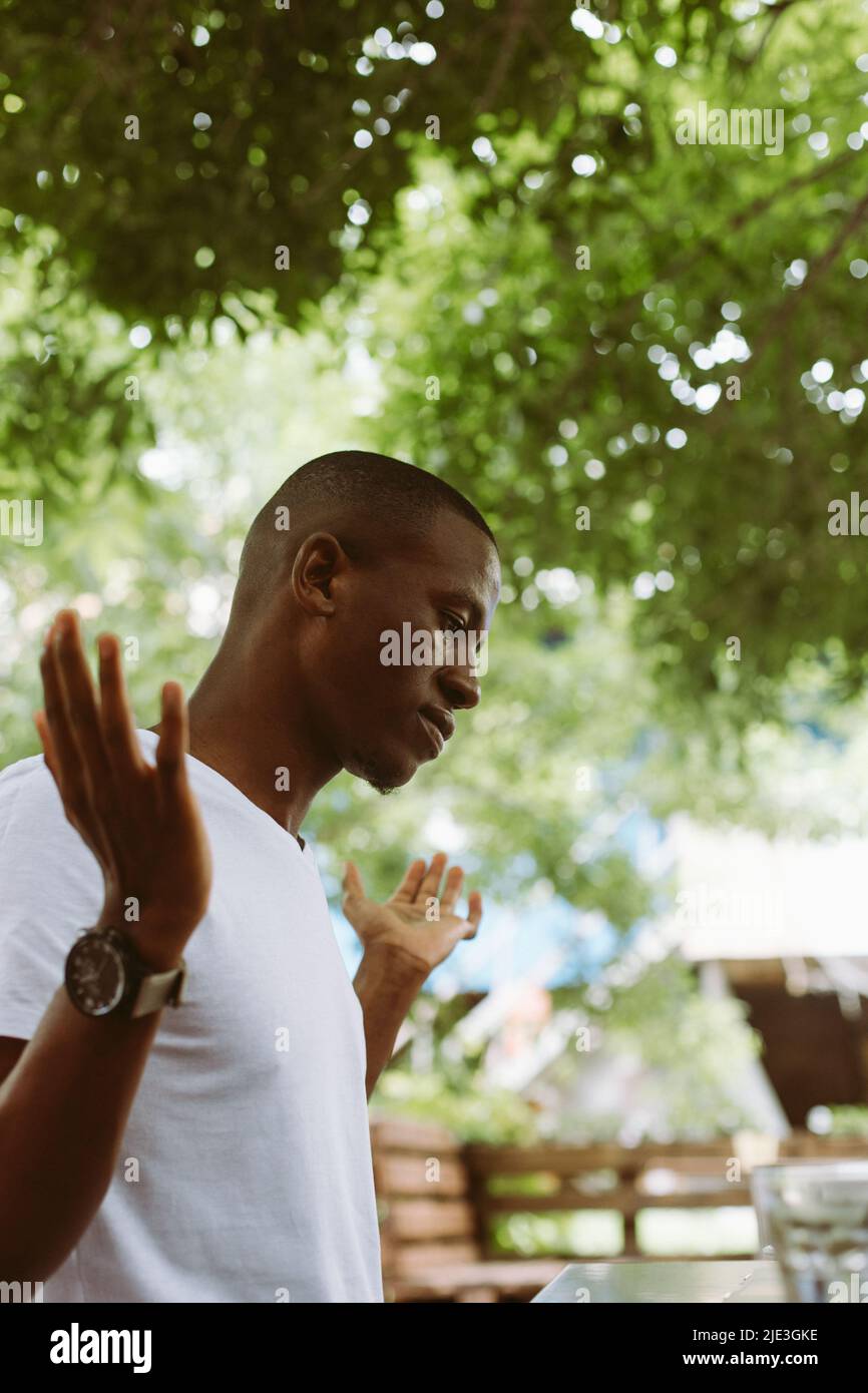 Surprised and confused african afro american man with laptop in cafe dont know what to do, raising hands in outdoor cafe Stock Photo