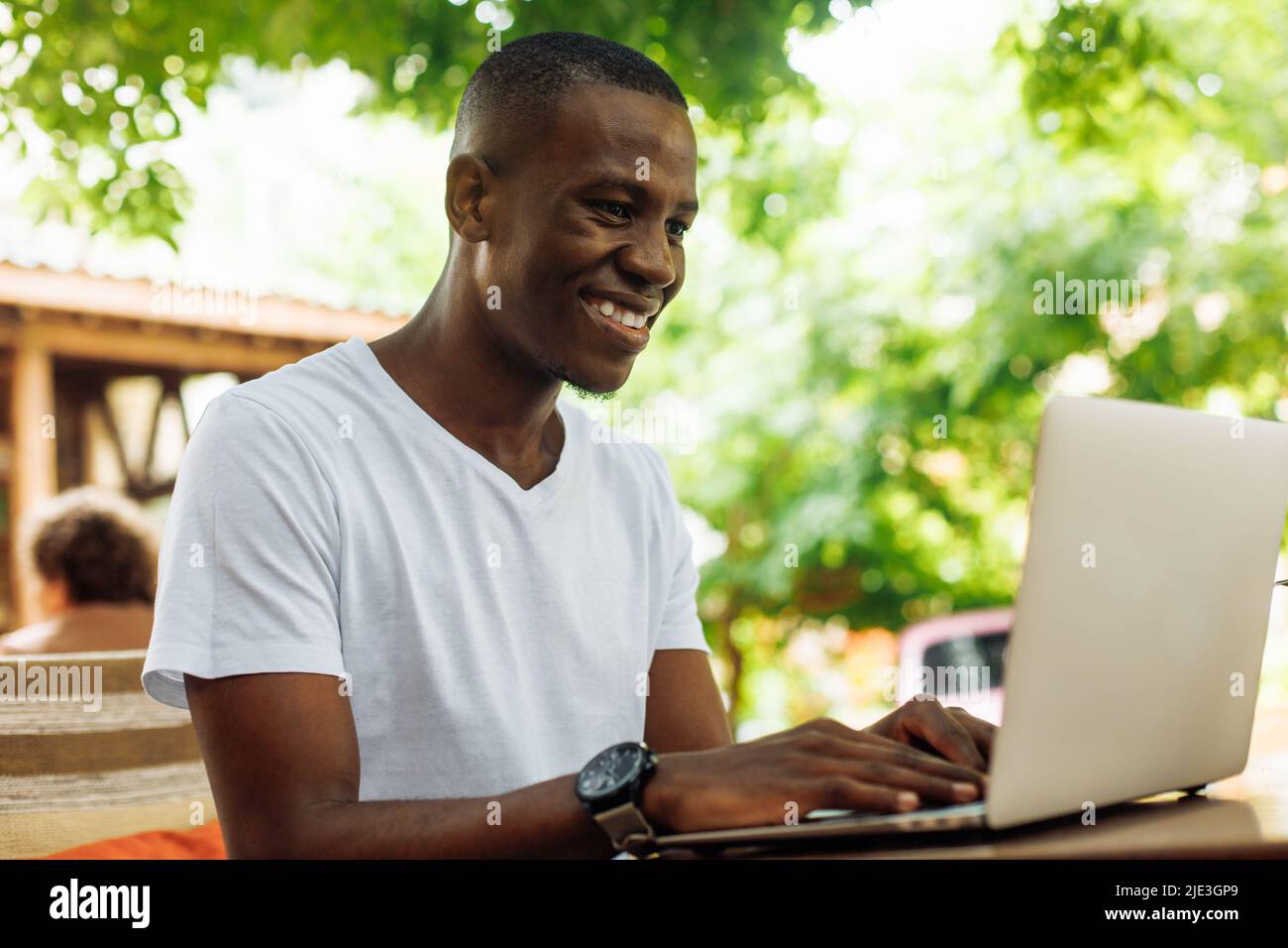 Closeup of laughing mixed race businessman, using laptop, working online as freelance technology worker in street cafe. Stock Photo