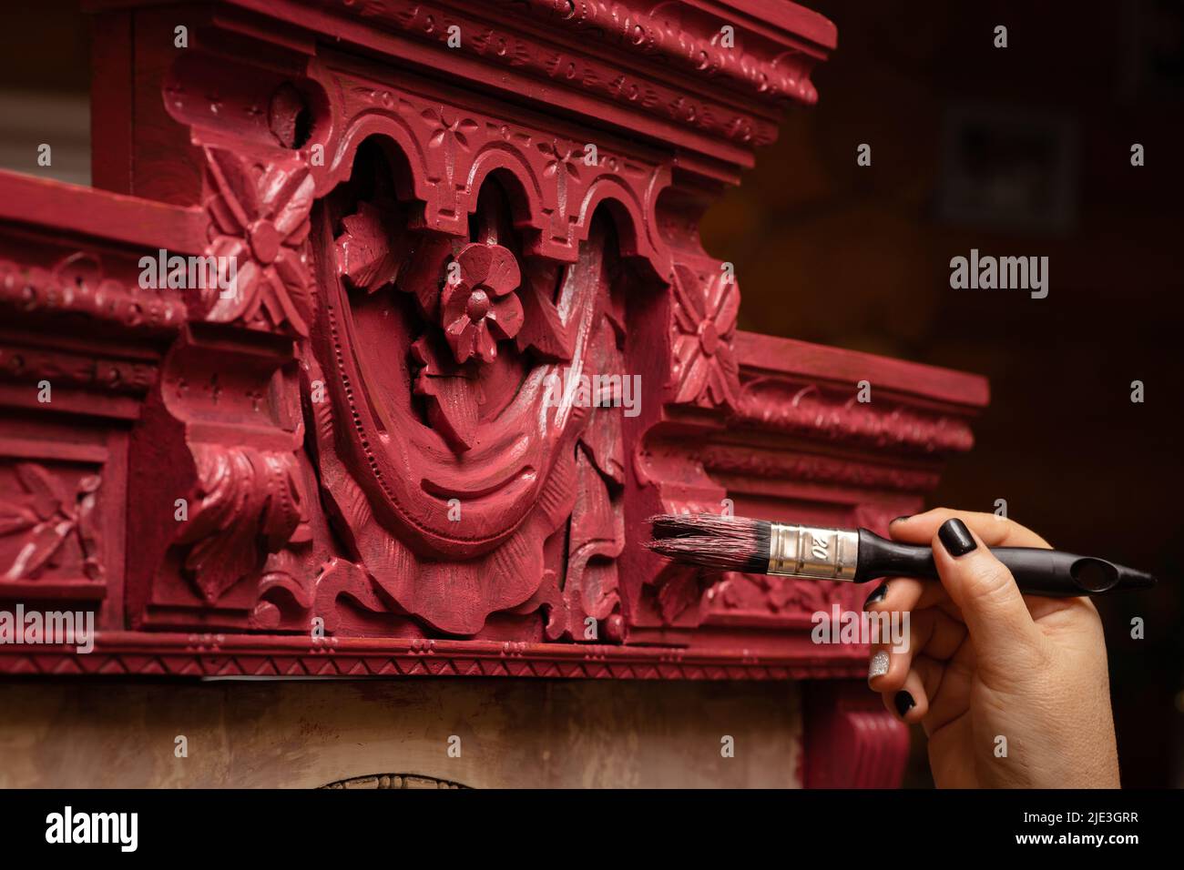 Woman aging wooden antique cupboard ornaments with big paint brush in workshop for renovation. Giving new life to old stuff. Hand restoration of old Stock Photo