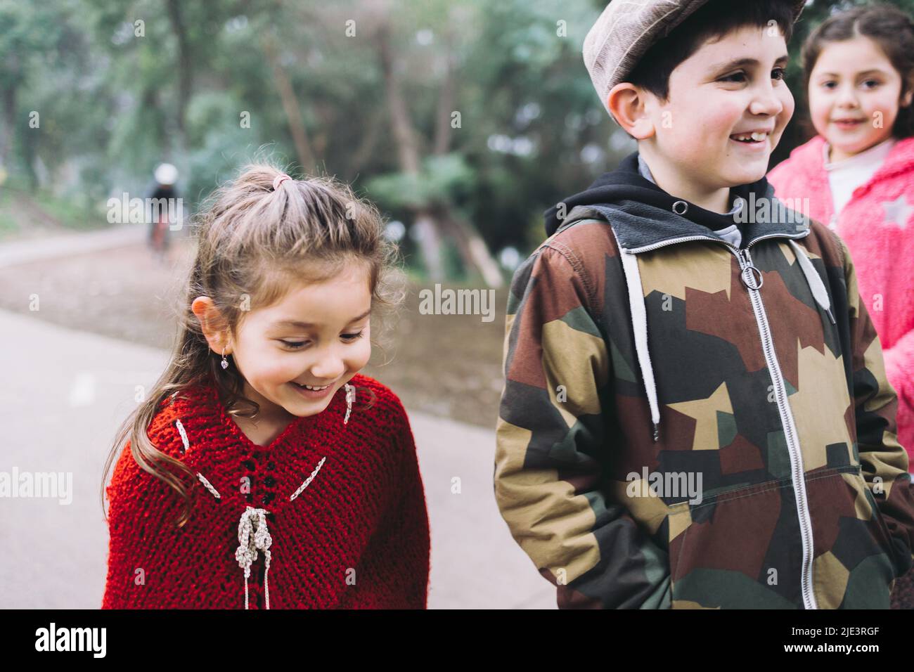 Three kids, tow girls and one boy, walking and talking in a park road.  Stock Photo