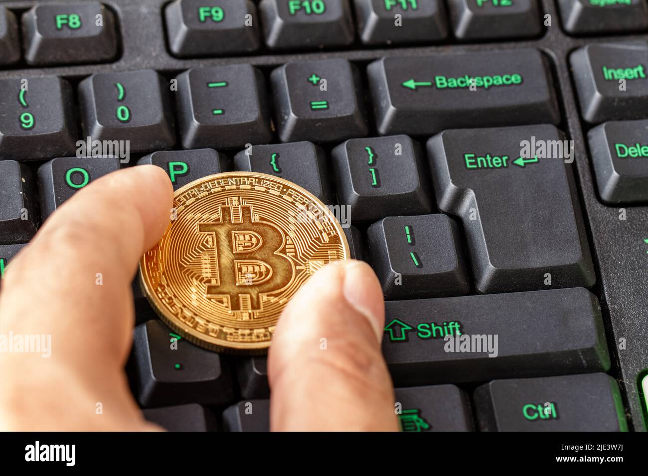 Hand holding bitcoin lying on computer keyboard, cryptocurrency for digital payment Stock Photo