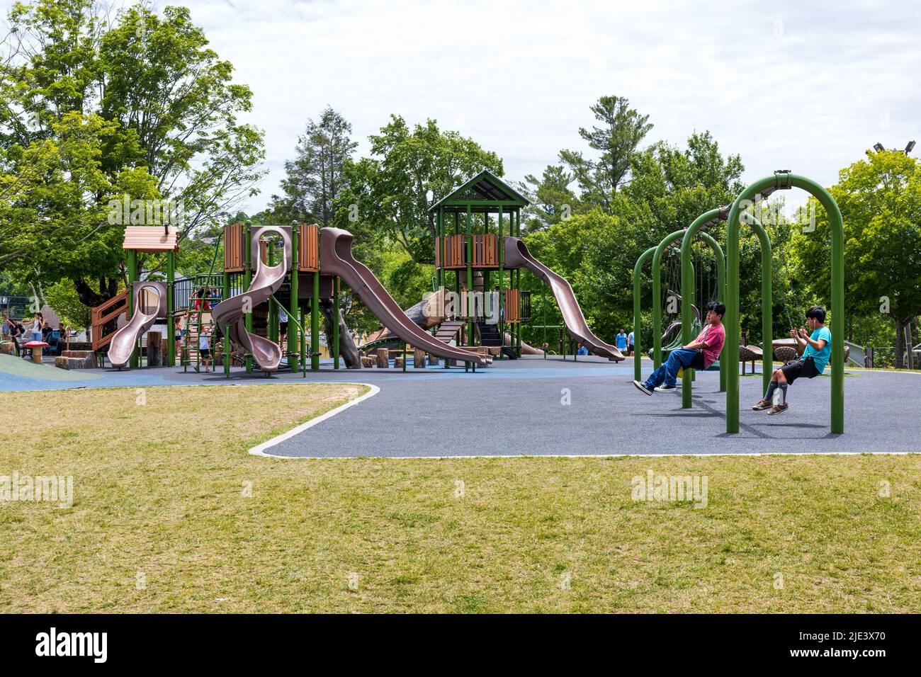 BLOWING ROCK, NC, USA-20 JUNE 2022: Playground in City Park, two boys play on swings, playground equipment and children in background. Stock Photo
