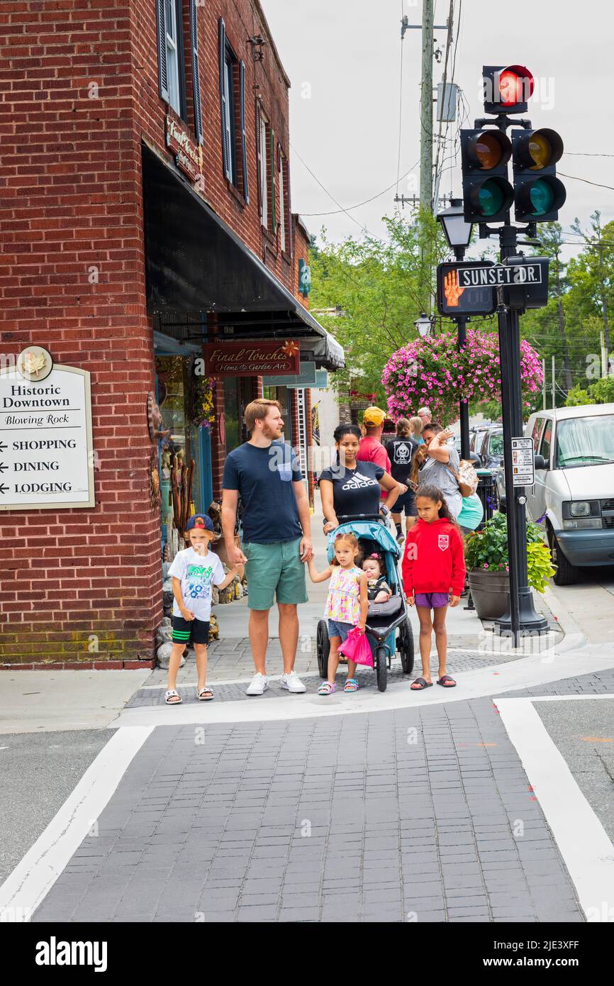 BLOWING ROCK, NC, USA-20 JUNE 2022: Biracial couple with children crossing Sunset Drive at Main St. Busy sidewalk behind. Stock Photo