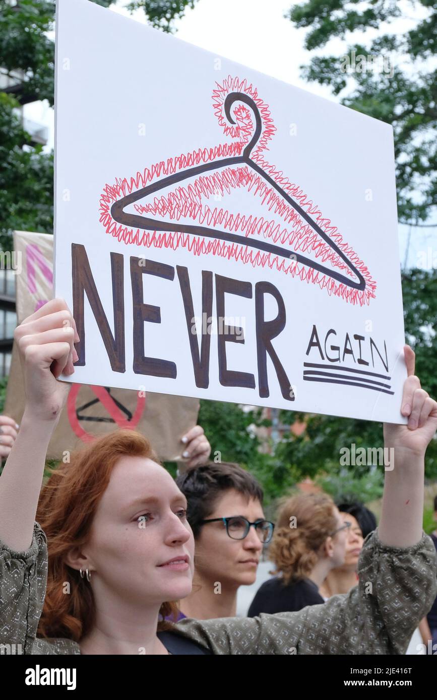 London, UK, 24th June, 2022. A woman holds a placard with a drawing of a coat hanger and the words, 'never again' as around 100-150 campaigners and supporters gathered to protest outside the American embassy in Vauxhall following the U.S. Supreme Court's decision to end the constitutional right to abortion - in place for almost 50 years following the 1973 Roe v Wade ruling.  Individual states will decide how to proceed, with thirteen automatically banning the medical procedure outright as trigger laws took effect. Credit: Eleventh Hour Photography/Alamy Live News Stock Photo