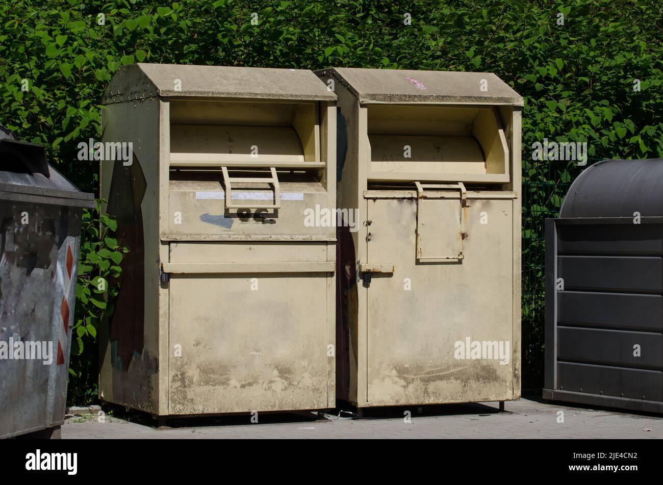 two dirty charity collection bins / clothing banks for the collection of old and used clothes and shoes standing at a recycling point Stock Photo