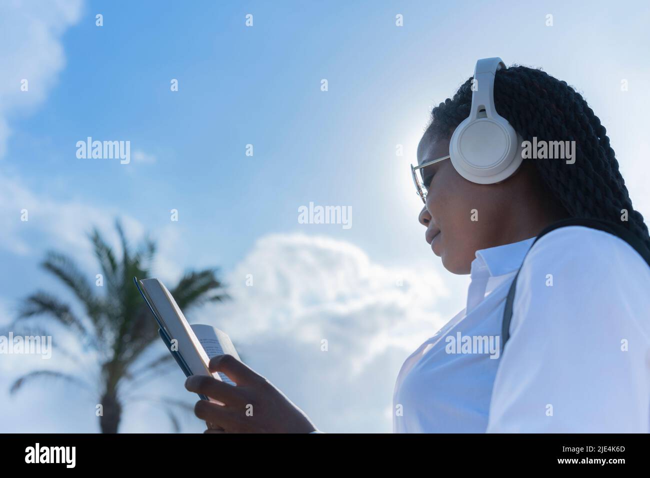 Focused african woman wearing headphones reading a book Stock Photo