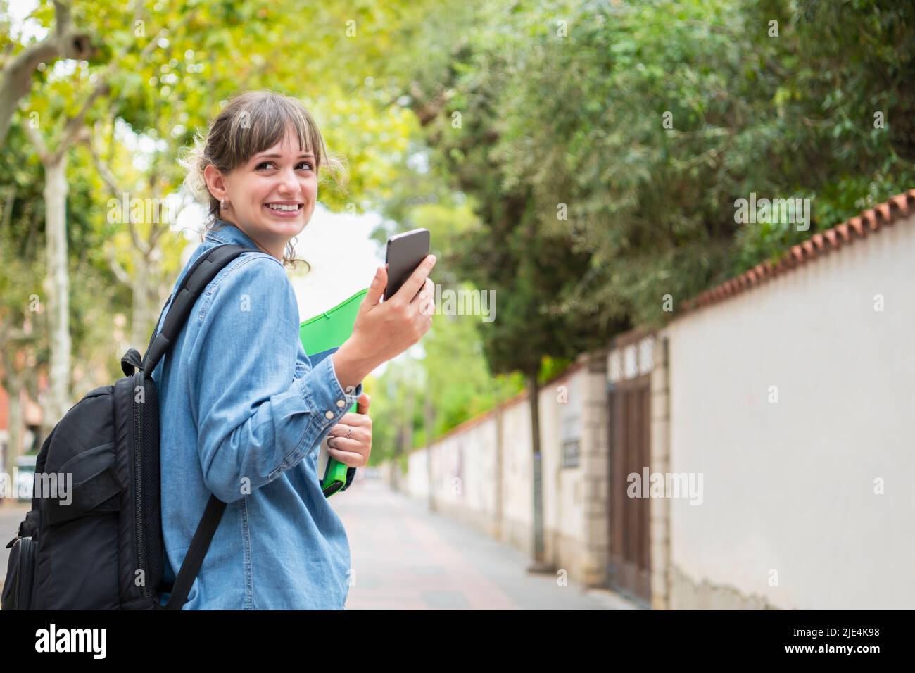 Young female student holding a phone looking back Stock Photo