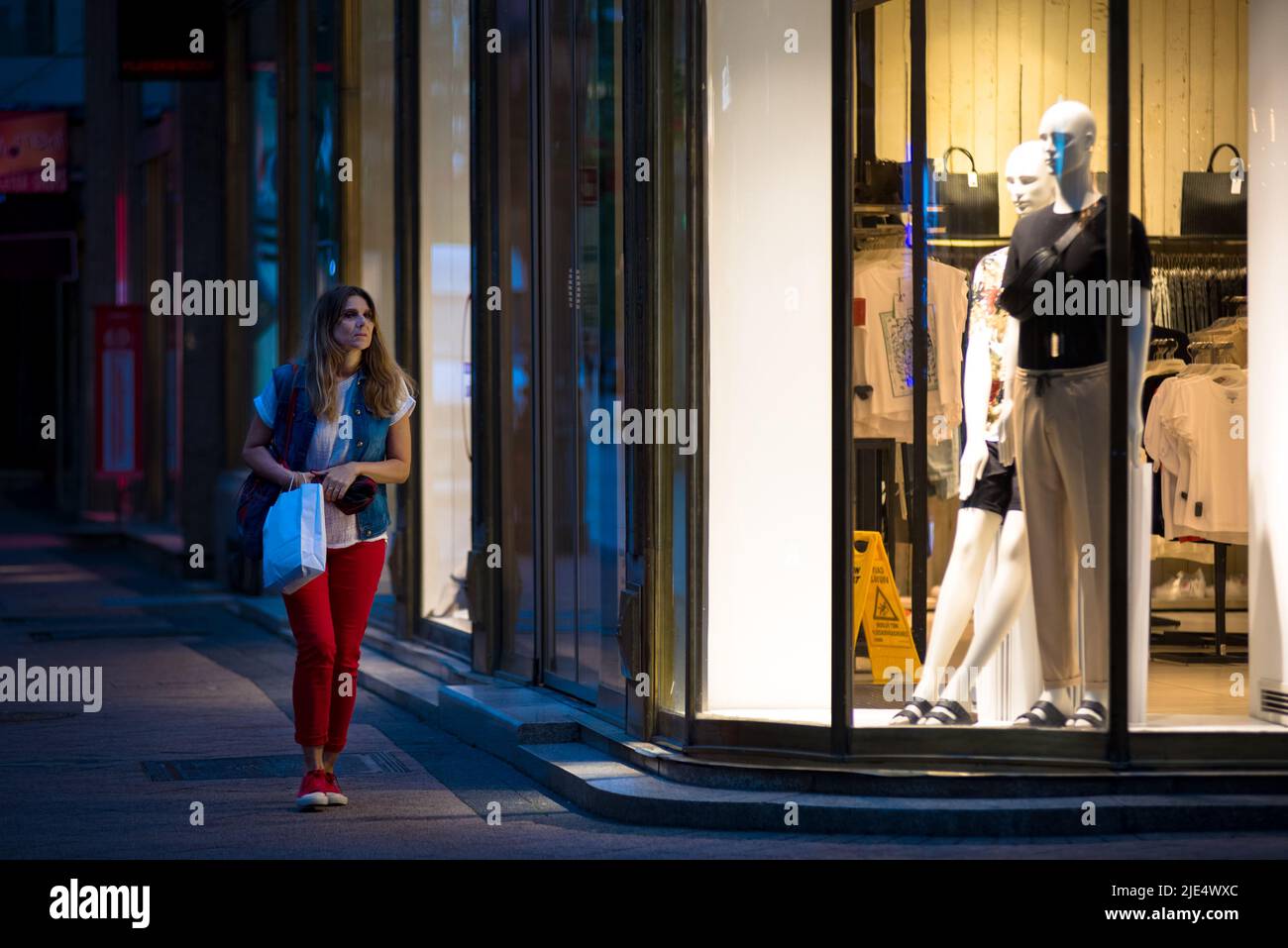 Woman passing shop window at night Stock Photo