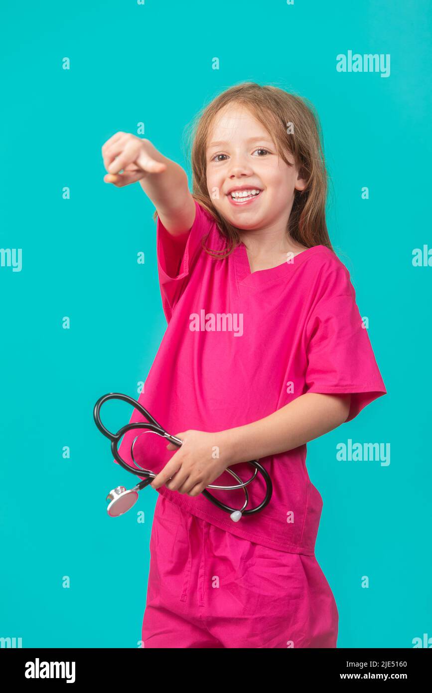 A 6-year-old girl is dressed as a doctor or nurse holds a stethoscope and points at the camera. Feminism, STEM, and healthcare concepts. Stock Photo