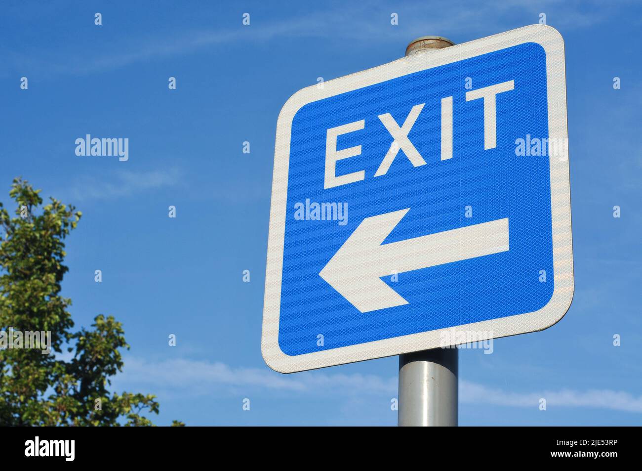 Low angle view of blue and white EXIT road sign with directional arrow symbol pointing to the left hand side, against a bright blue sky background. Stock Photo
