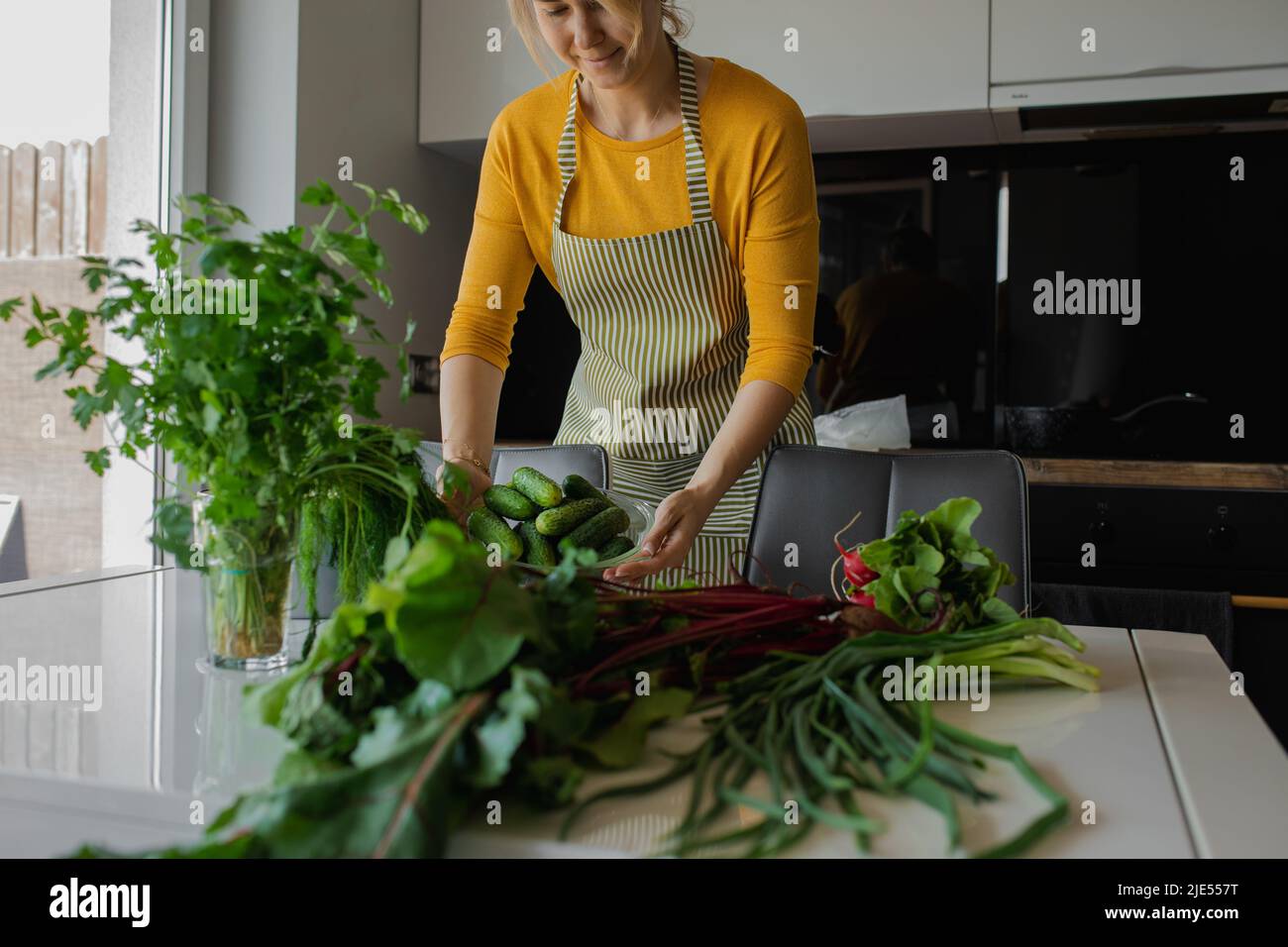 Blond woman in apron cooking healthy fresh vegetable salad in the home kitchen. Organic farming dish for loosing weight Stock Photo