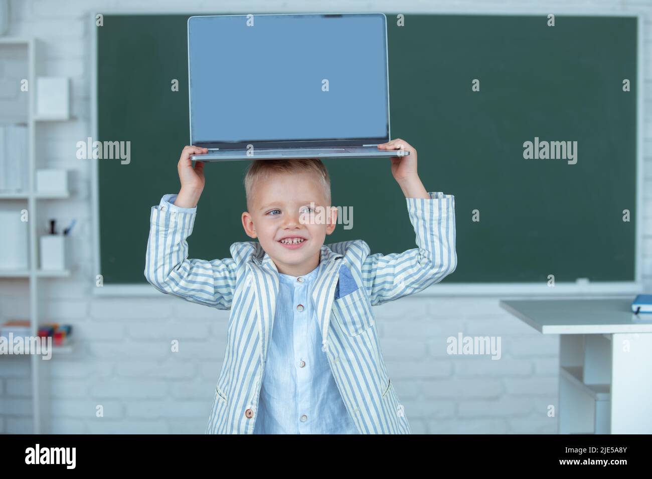 Kid boy holding laptop on head, learning lesson at school, using gadget