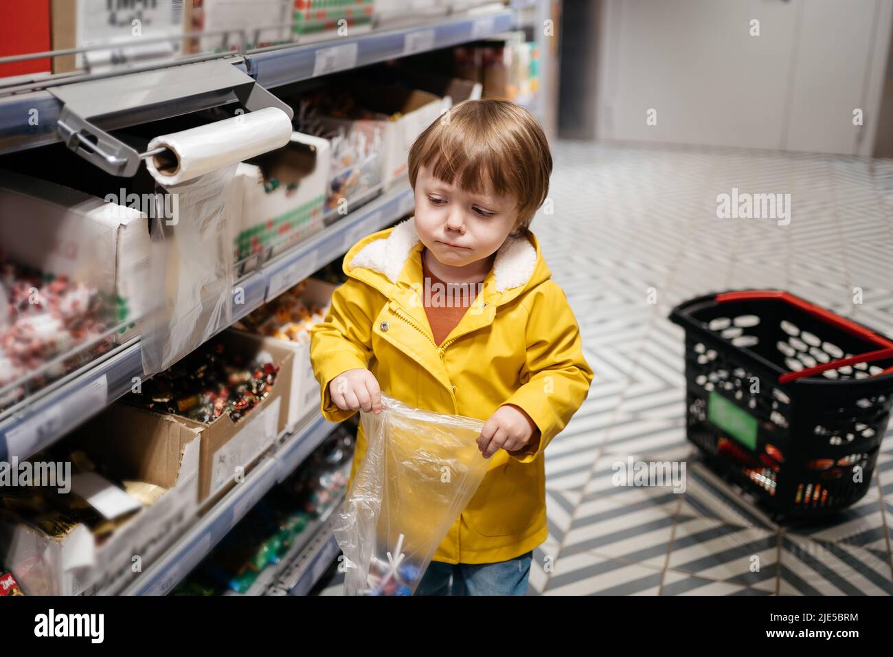child in the market with a grocery cart, puts sweets in a bag Stock