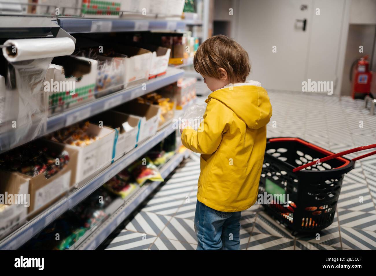 child in the market with a grocery cart, puts sweets in a bag Stock