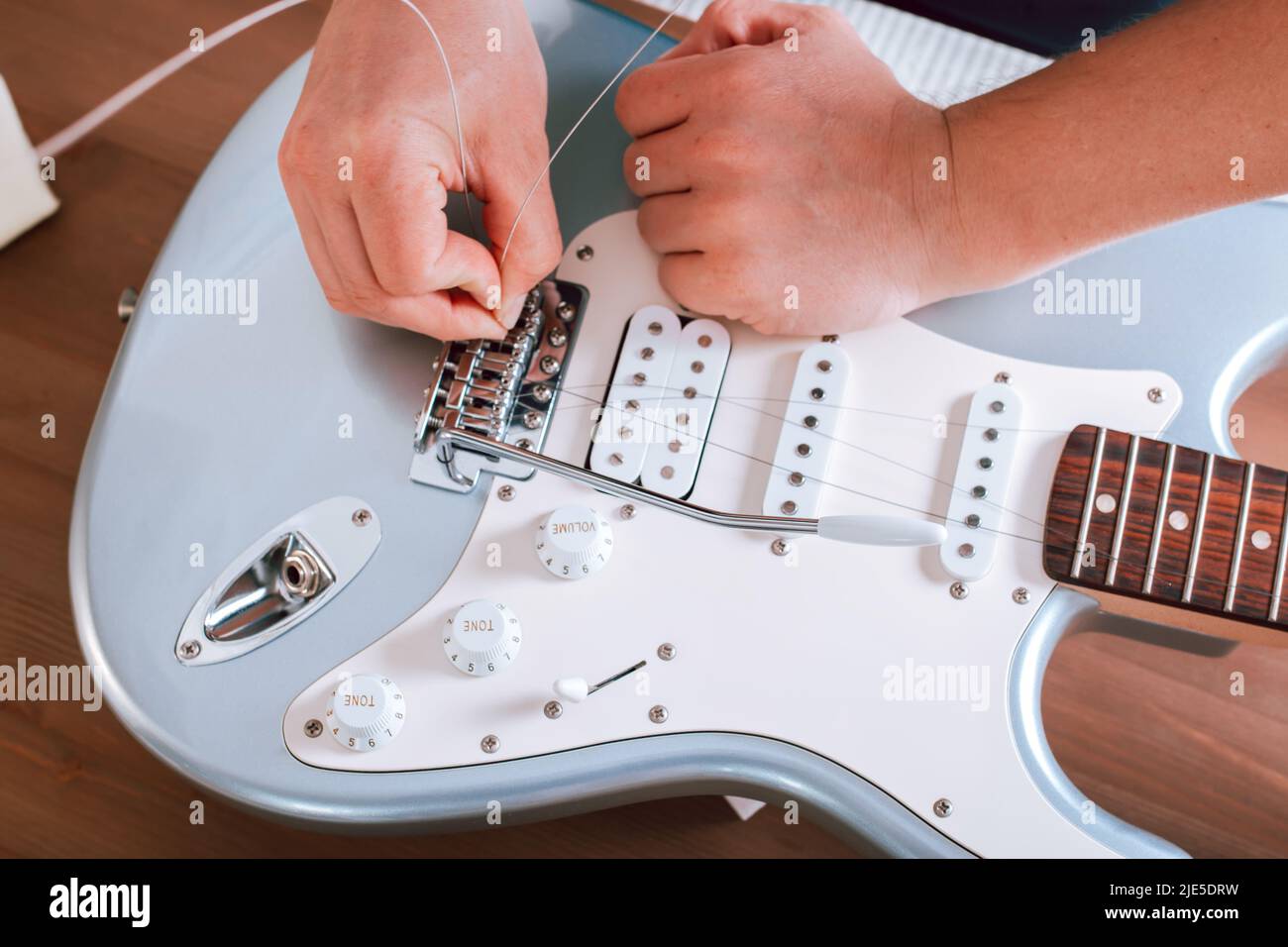 Guitar master restringing electric guitar, top view, hands closeup