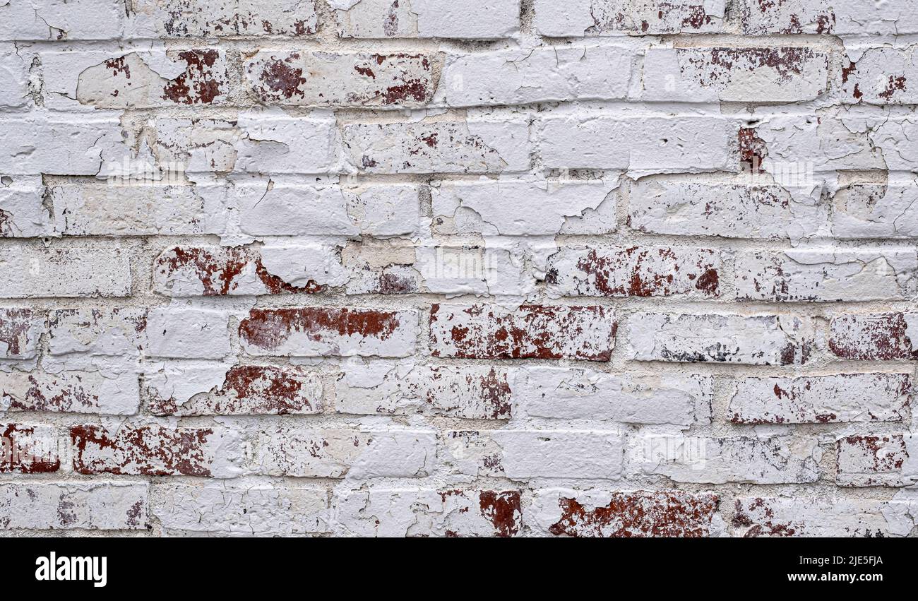 Red brick wall covered in peeling white paint grunge texture Stock
