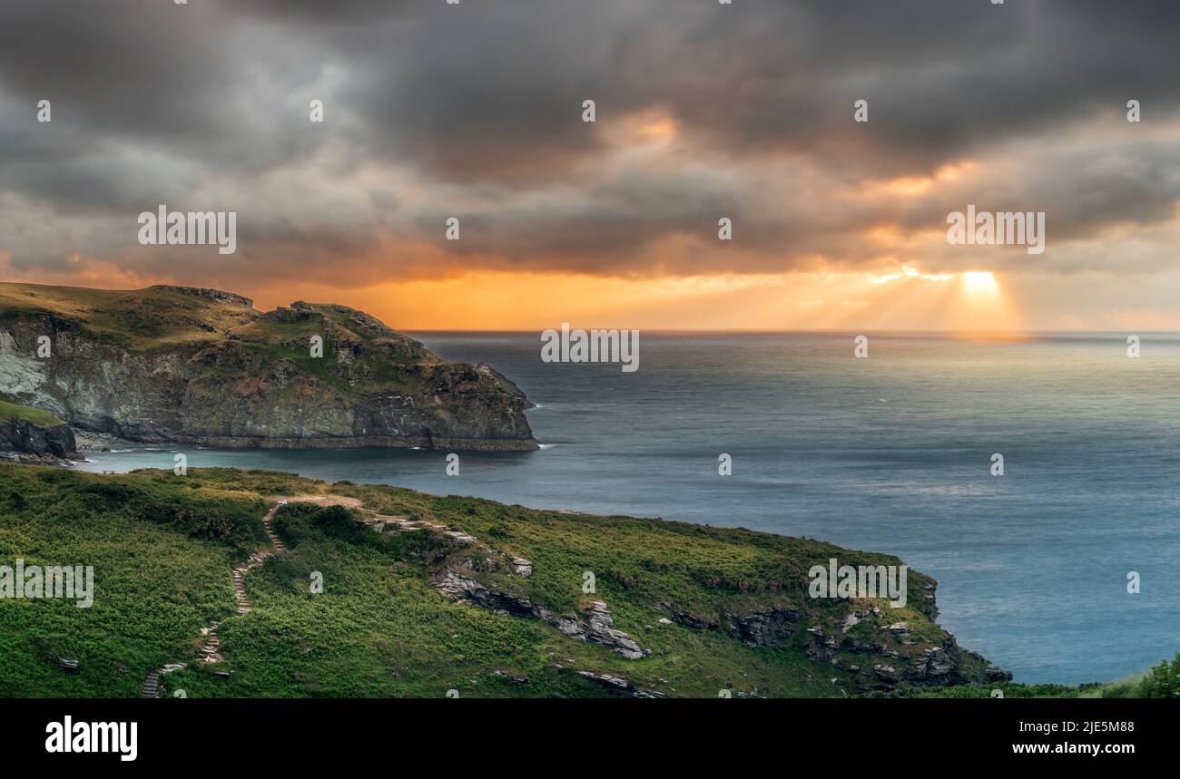 A dramatic sunset at the end of a stormy day in North Cornwall as the sun sets over the coastal footpath and Rocky Valley at Trethevy near Tintagel. Stock Photo