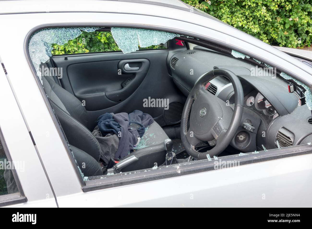 A car with its drivers side window smashed after being attacked by a thief. Shattered glass from the window is shown on the seats inside the insecure vehicle Stock Photo