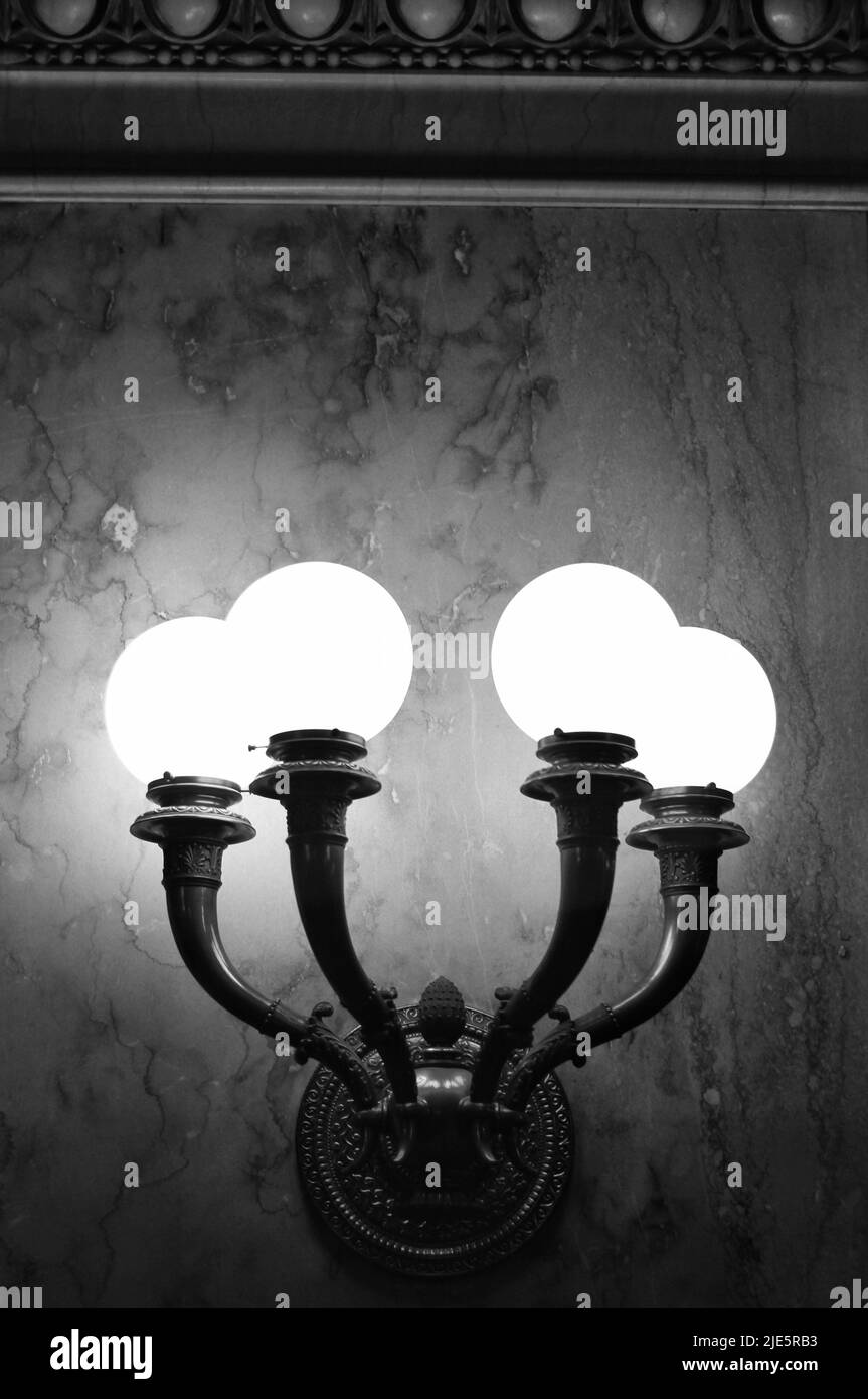 Beautiful vintage traditional illuminating wall sconces hanging on the wall and glowing with light in black and white. Stock Photo