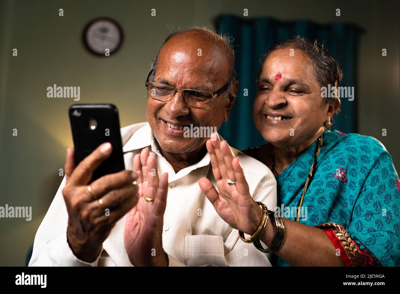 happy senior couple busy on making video call using smartphone at home - concept of technology, bonding and connection Stock Photo