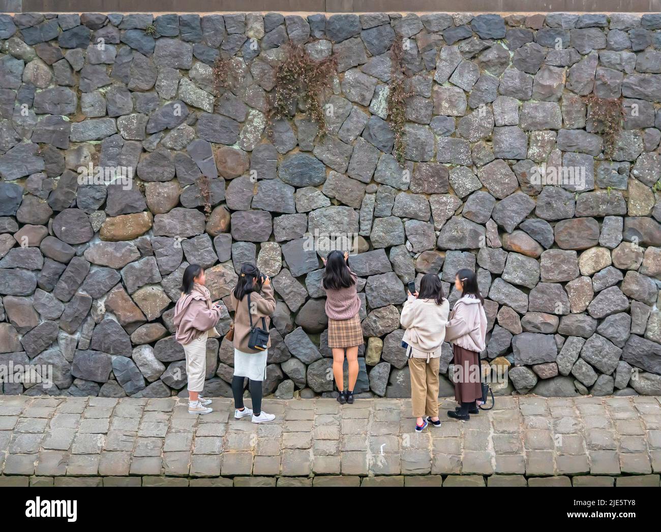 nagasaki, kyushu - december 12 2021: Young tourists girls taking photos and praying for eternal love in front of a heart shaped stone along the bank o Stock Photo