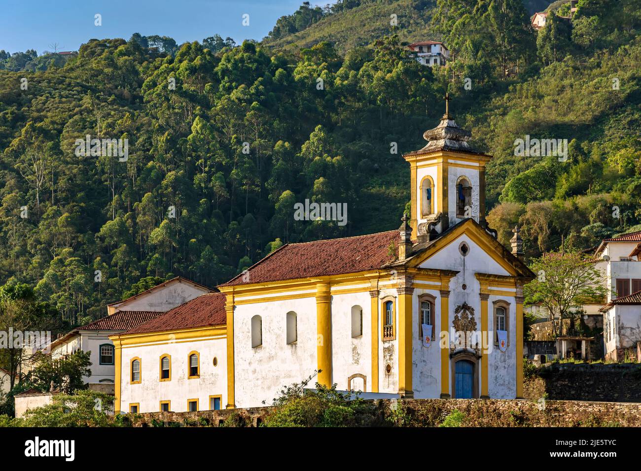Facade of a historic baroque-style church in the city of Ouro Preto in Minas Gerais illuminated during the late afternoon with the hills and local veg Stock Photo