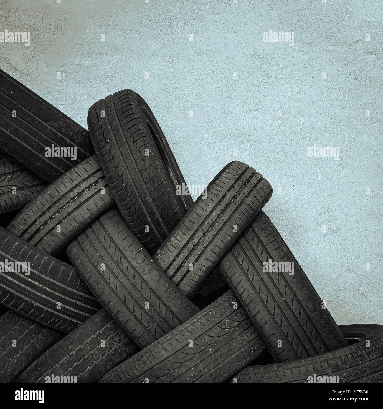 A monochrome image of a stack of used interwoven car tyres against a blank wall ready for dumping or recycling Stock Photo