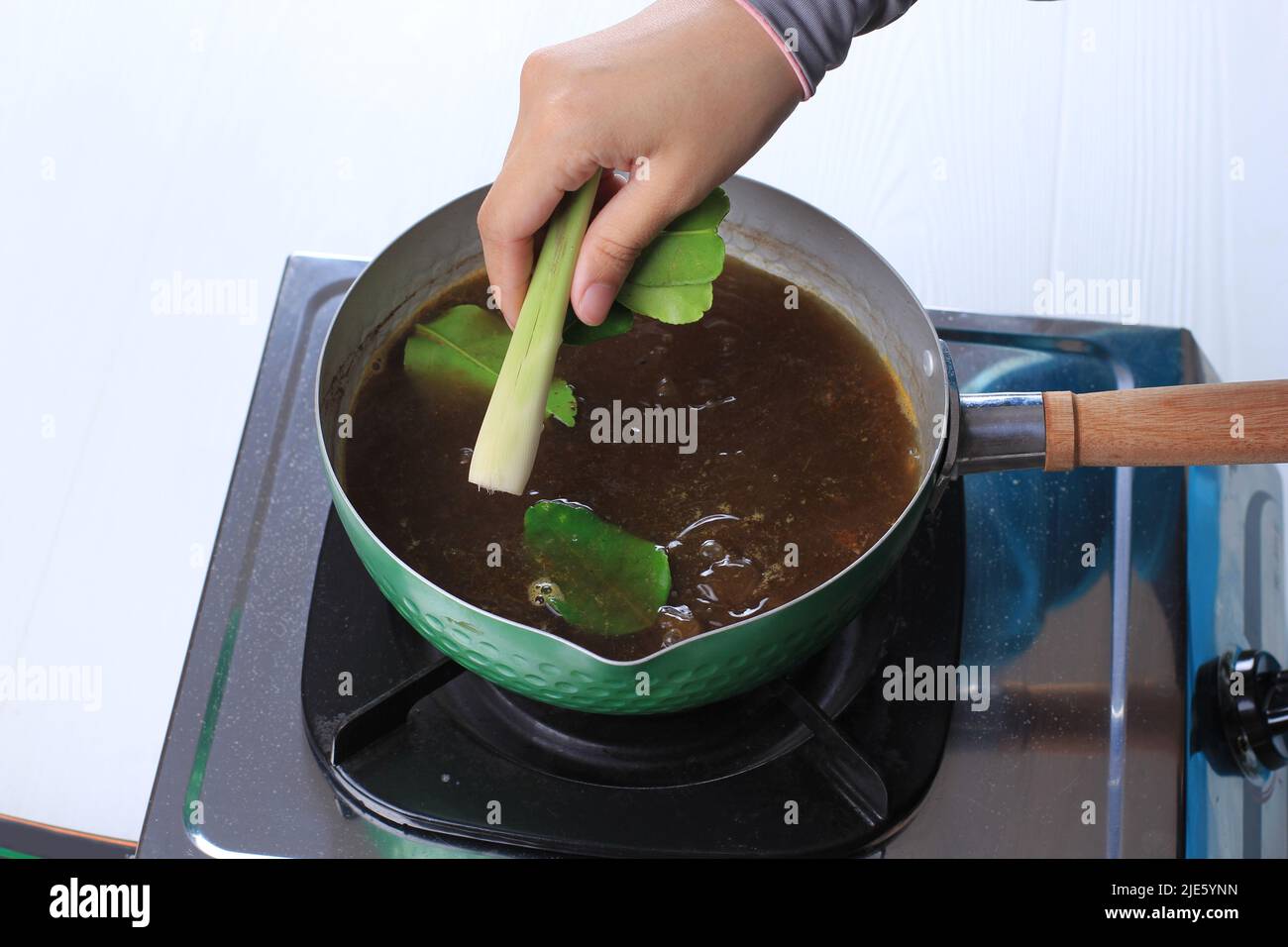 Female Chef Add Lime Leaf and Lemongrass, Cooking Process Making Rawon, Indonesian Beef Black Soup. Cooking Backstage in the Kitchen Stock Photo
