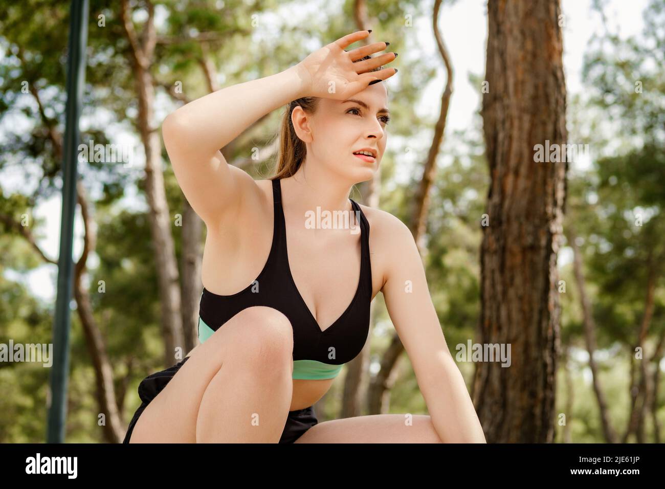 Young beautiful woman wearing sportive clothes on city park, outdoors after jogging catching her breath, wiping her sweat from her forehead. Stock Photo