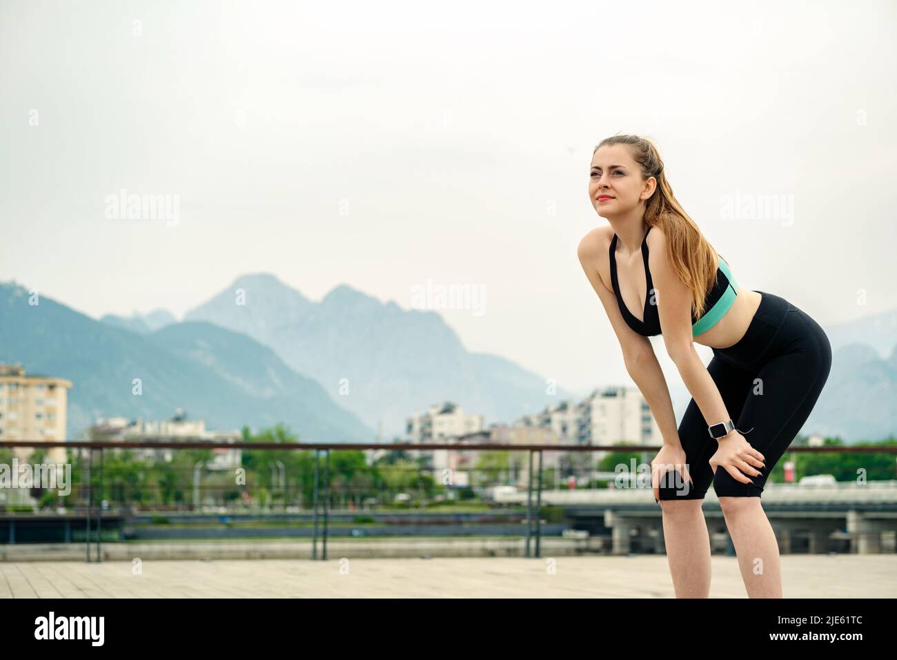 Young beautiful woman wearing sportive clothes on city park, outdoors standing bent over and catching her breath after a running session. Outdoor spor Stock Photo