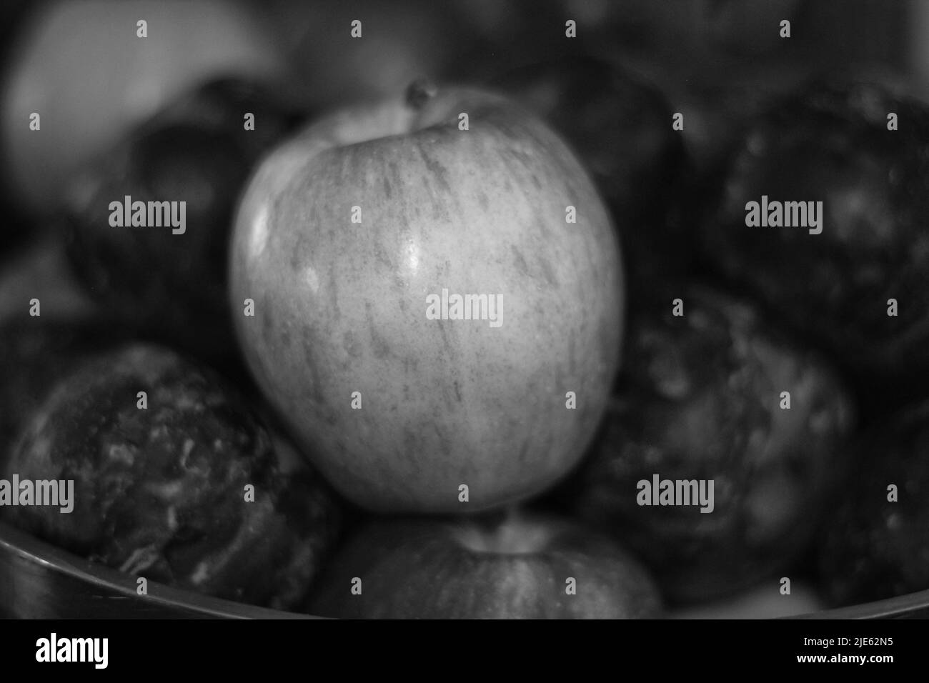 Delicious apple sitting among a bunch of tasty plums in a fruit bowl in black and white. Stock Photo