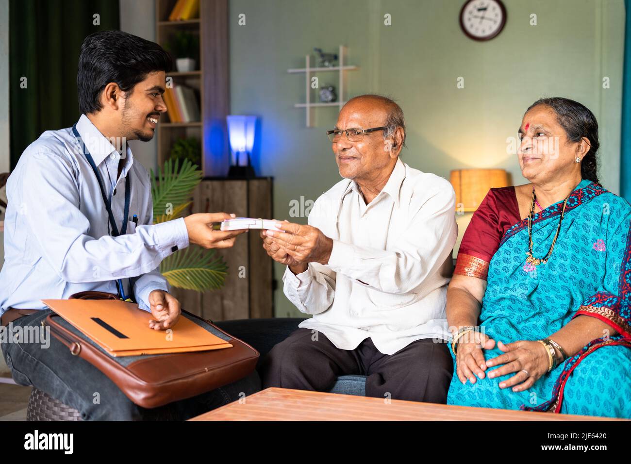 Happy smiling senior couple receiving stack of money from bank officer or insurer at home - concept of insurance claim and home banking support Stock Photo