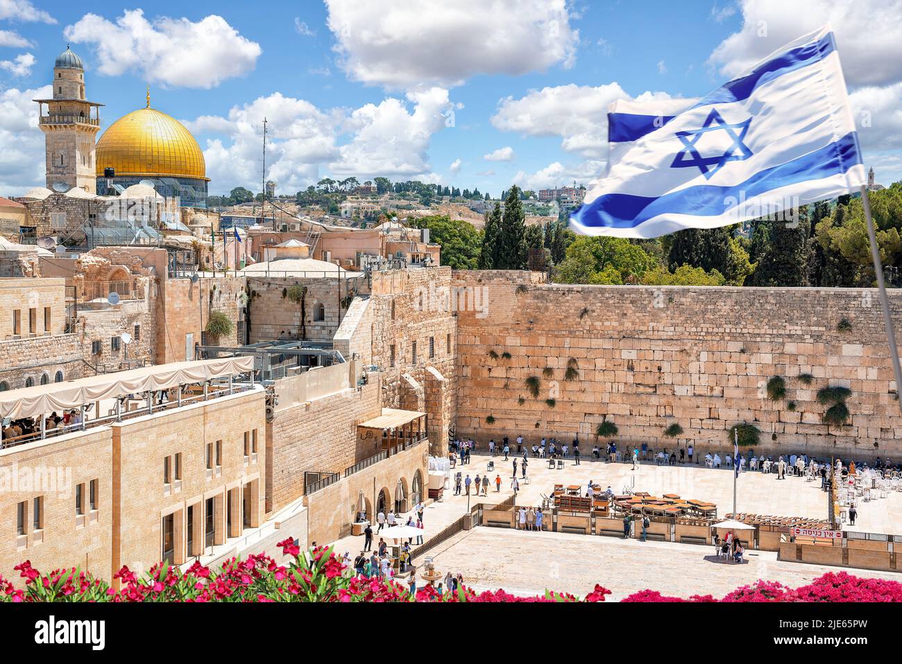 Jerusalem, Israel; June 25, 2022 - An Israeli flag blows in the wind as jewish orthodox believers read the Torah and pray facing the Western Wall, in Stock Photo
