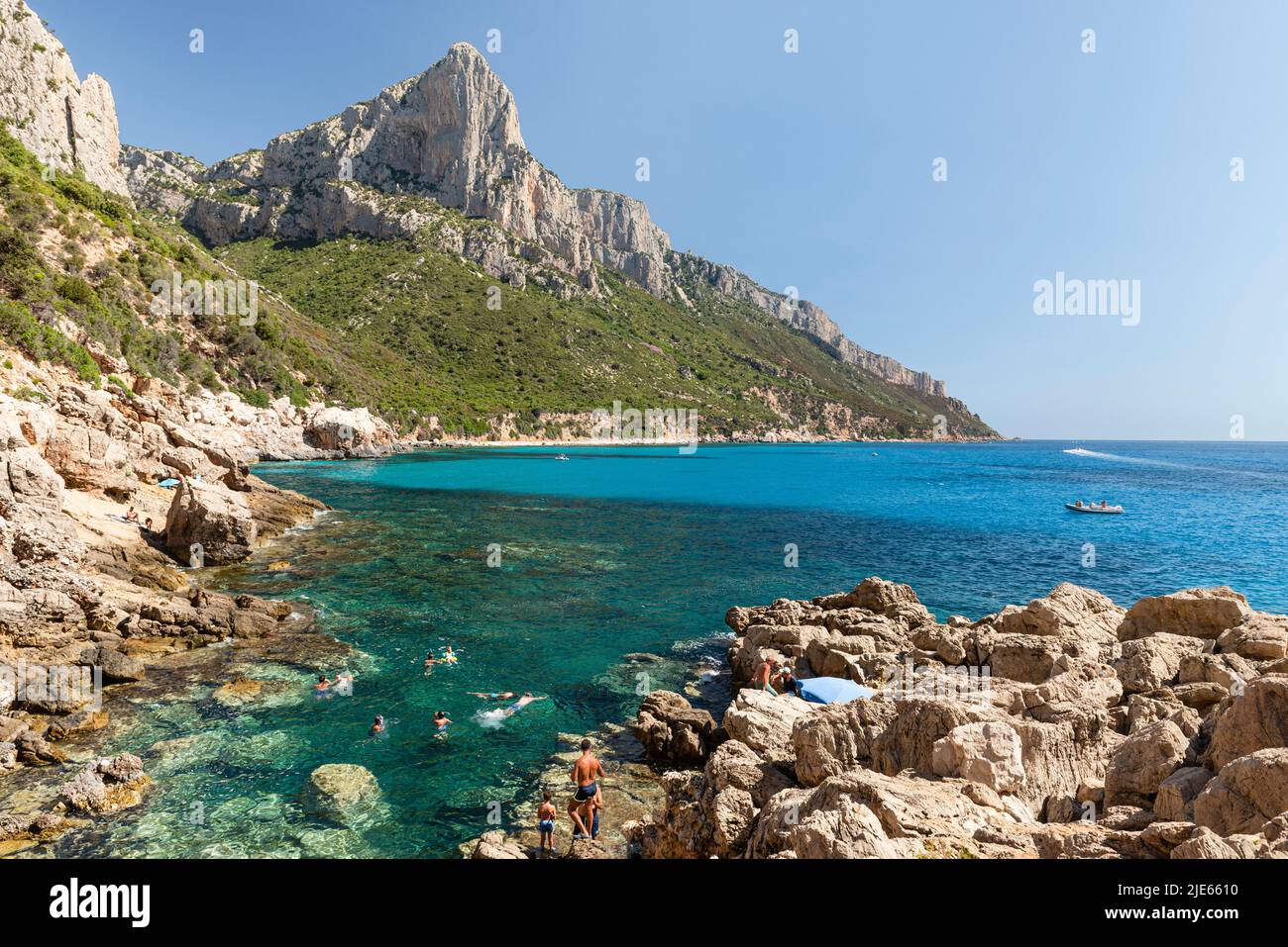 Swimmers in the turquoise sea on the cliff below the rocky walls of Punta Giradili on the east coast of Sardinia, shining in the morning sun Stock Photo