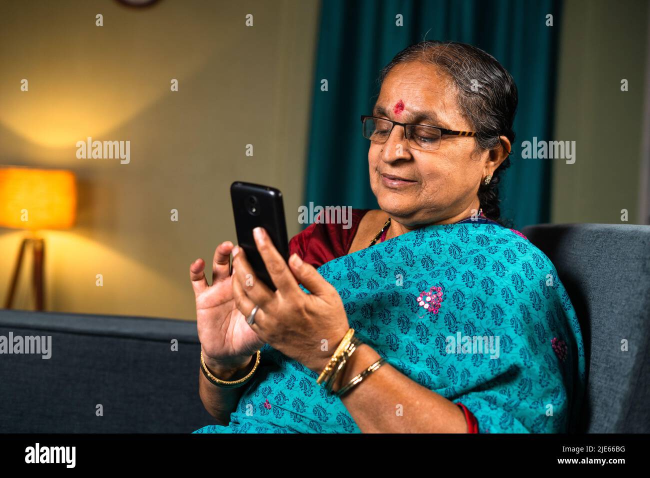 Senior woman busy using mobile phone while sitting on sofa at home - concepts of technology, relaxation and social media Stock Photo