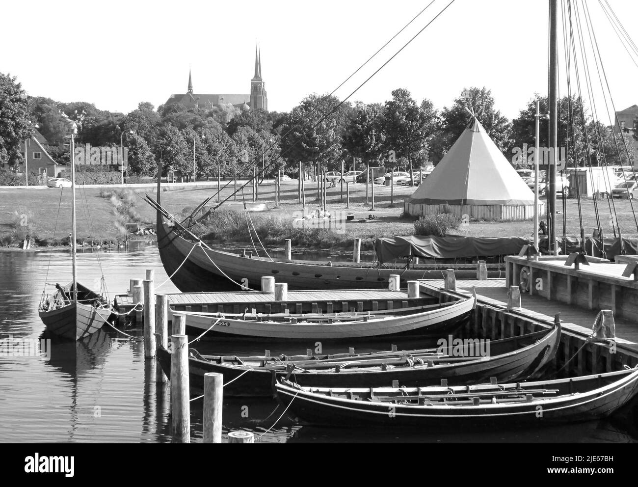 Monochrome Image of Moored Boats at the Viking Ship Museum's Pier with St. Luke Cathedral in the Backdrop, Roskilde, Denmark Stock Photo